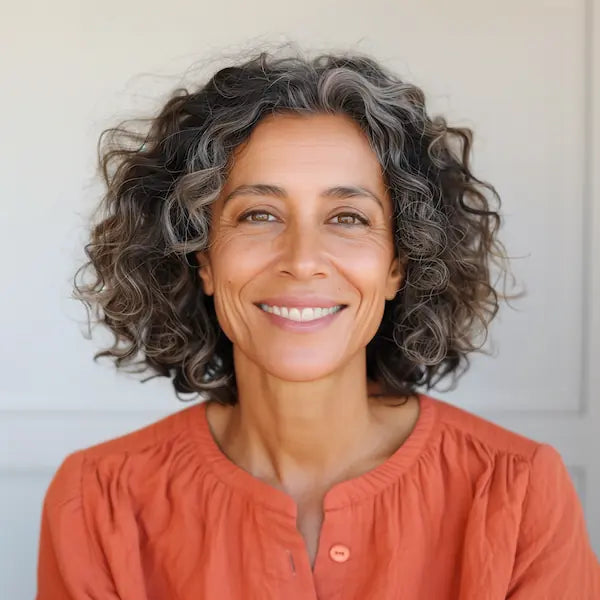 Retrato de una mujer mexicana de mediana edad sonriendo mientras comparte su experiencia con la Cruz Premium de Élite Luxe. Testimonio de una clienta satisfecha que recomienda el collar para hombre en acero inoxidable 316L por su calidad, elegancia y significado. Joyería masculina premium para caballeros en México.